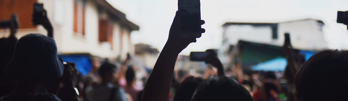 Image by SuHyeon Choi - a hand holds a phone above a crowd